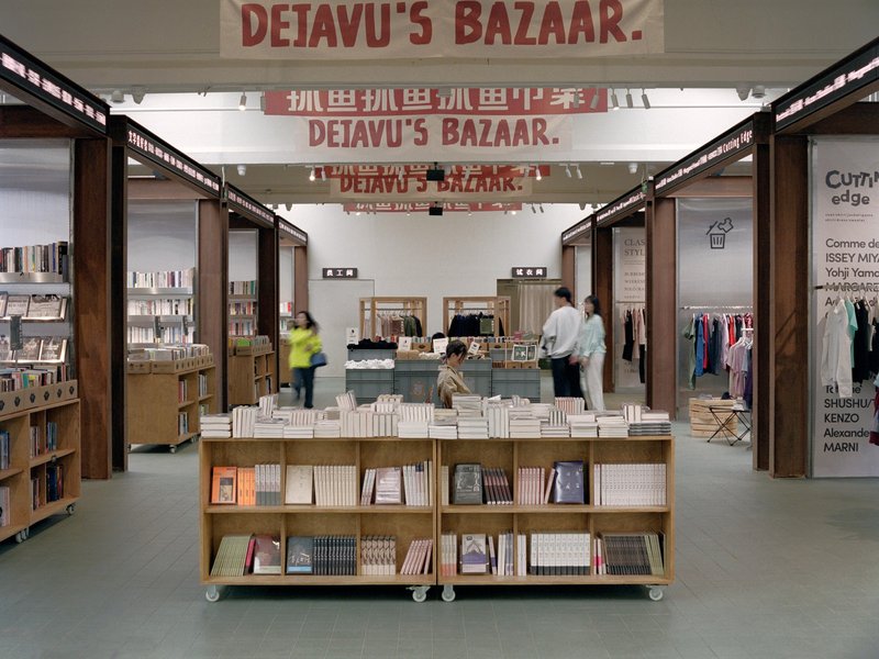 Interior view of retail space with timber-framed portals, wheeled book display units, and customers browsing under bright ceiling lights