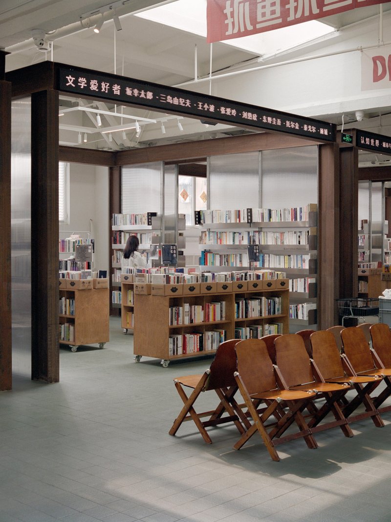 View into book retail area with timber portal frame, translucent panels, mobile shelving units, and folding canvas chairs