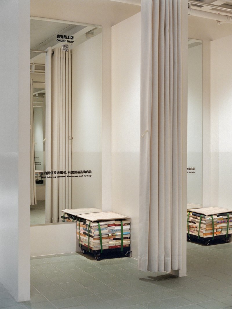 White curtain divider beside seating cube made from stacked recycled books on a wheeled base beneath mirrored panels