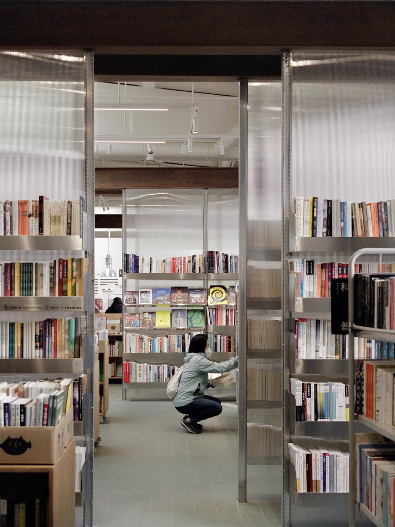 View through metal shelving units into the bookstore with a visitor crouching among the stacks