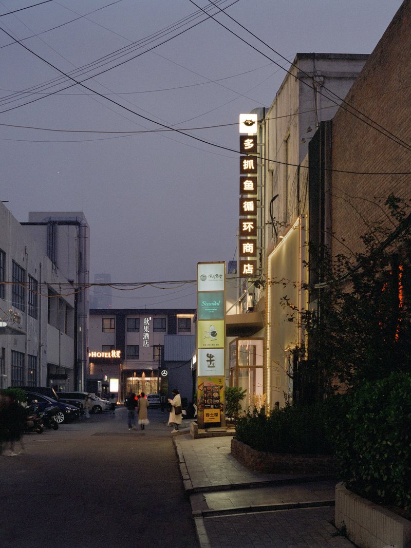 Narrow street view at dusk with illuminated storefronts and overhead power lines