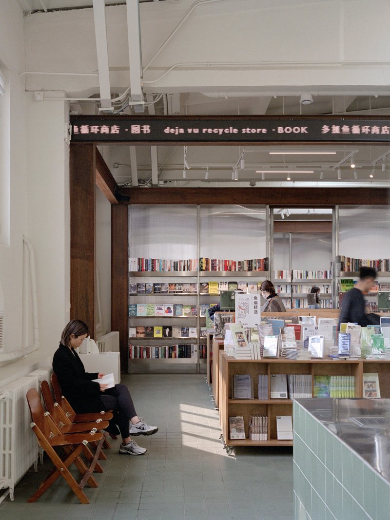 Interior reading area with exposed white ceiling structure and timber-framed bookshelves beyond folding chairs