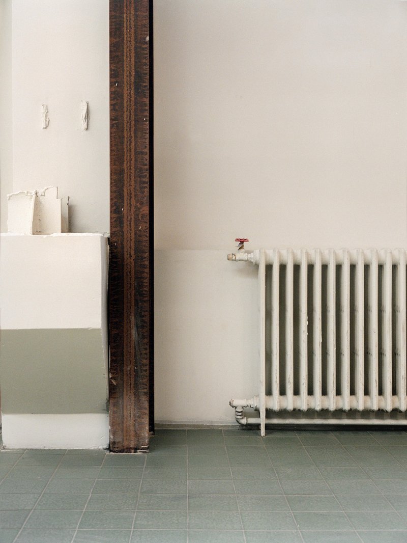 White radiator beside an exposed timber column and half-height partition on green tile flooring