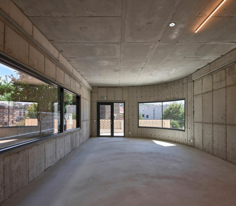 Interior room with board-formed concrete walls and ceiling illuminated by recessed linear lighting