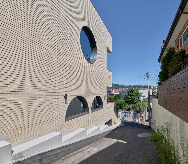 Street view of white brick facade with circular and arched windows along a narrow lane