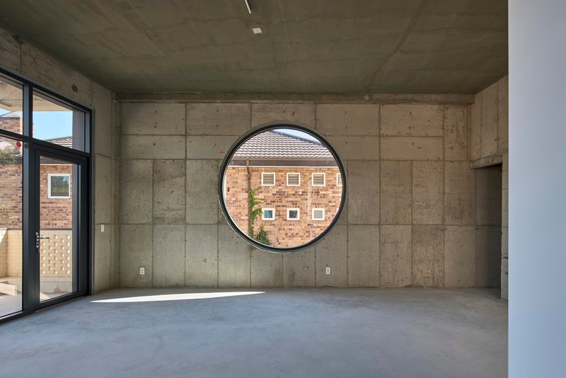 Interior room with board-formed concrete walls and a large circular window framing neighboring buildings