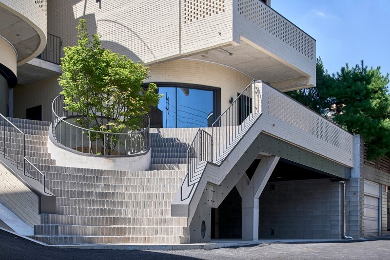 Curved planter with young tree on the tiled staircase leading to the angled garage entry