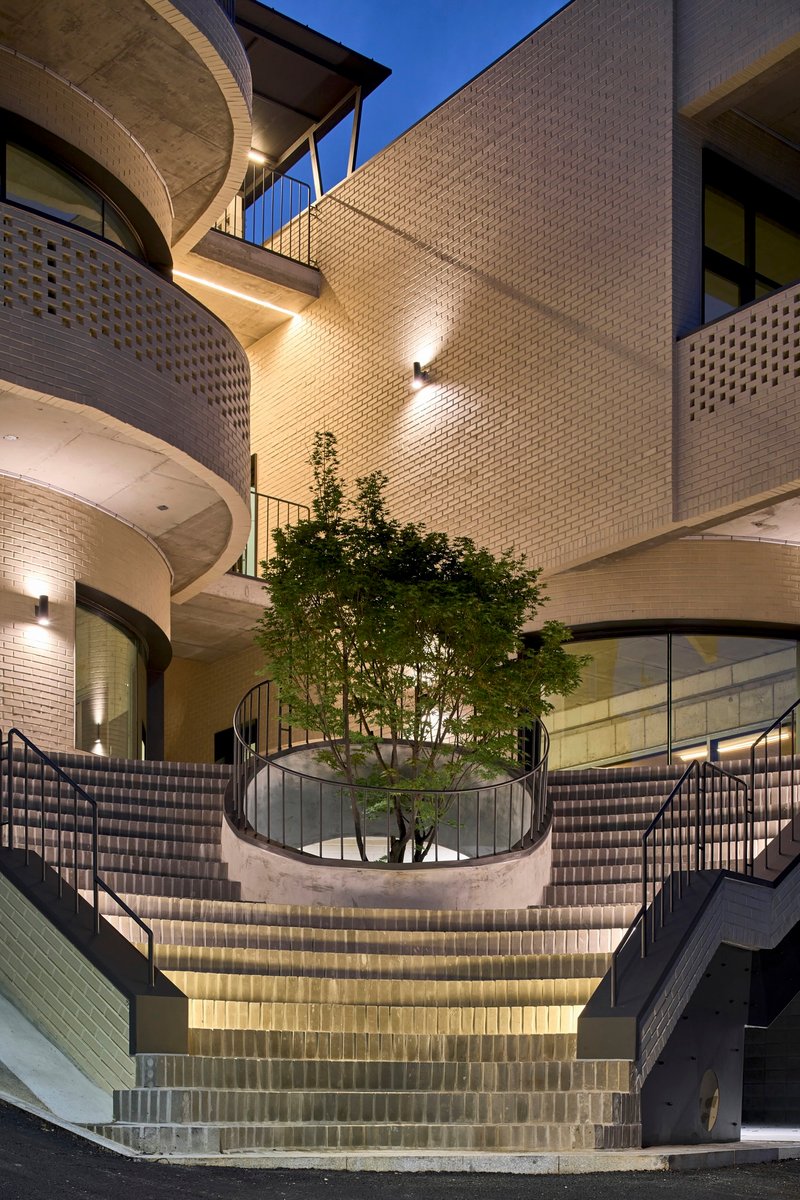 Curved exterior staircase descending to a courtyard with a central tree at twilight