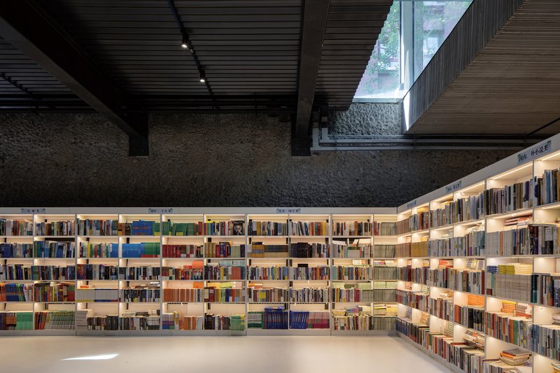 Library interior with illuminated bookshelves wrapping textured stone walls beneath a dark slatted ceiling