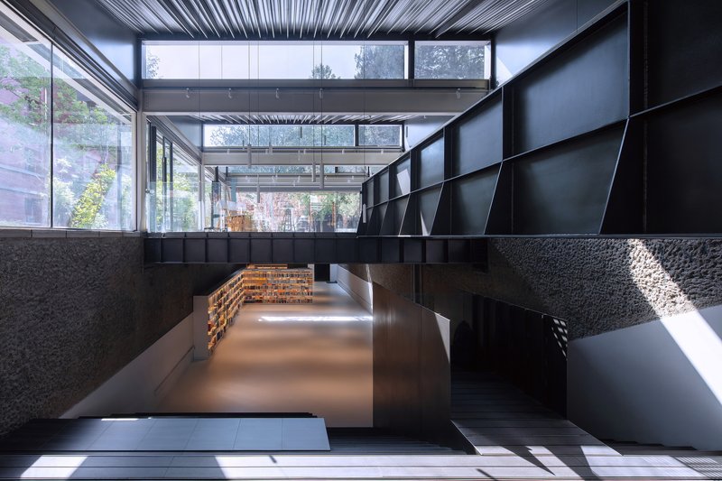 Multilevel interior with black metal staircase and bridge connecting spaces beneath continuous glazed clerestory windows