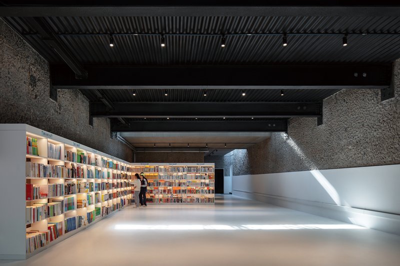 Interior reading room with backlit bookshelves and textured stone walls under a ribbed black ceiling