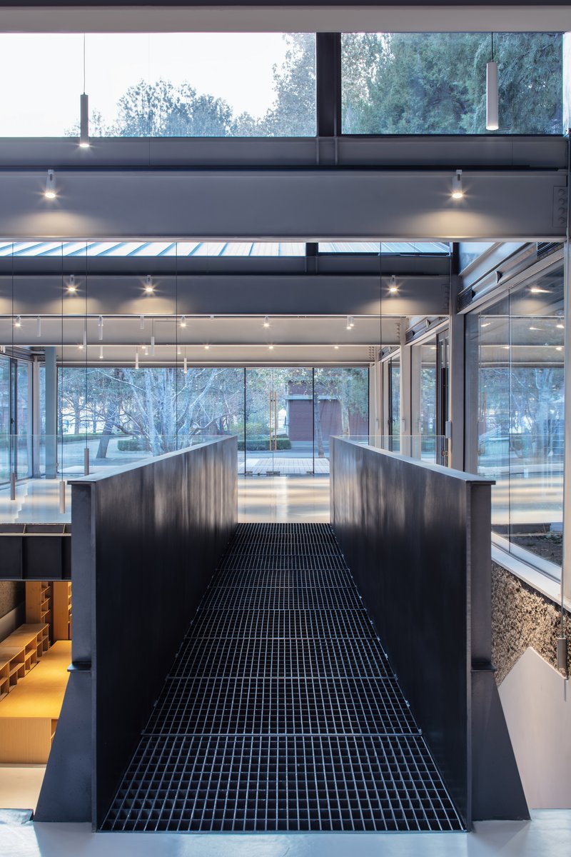 Central black grated bridge spanning between levels with full-height glazing overlooking exterior courtyard
