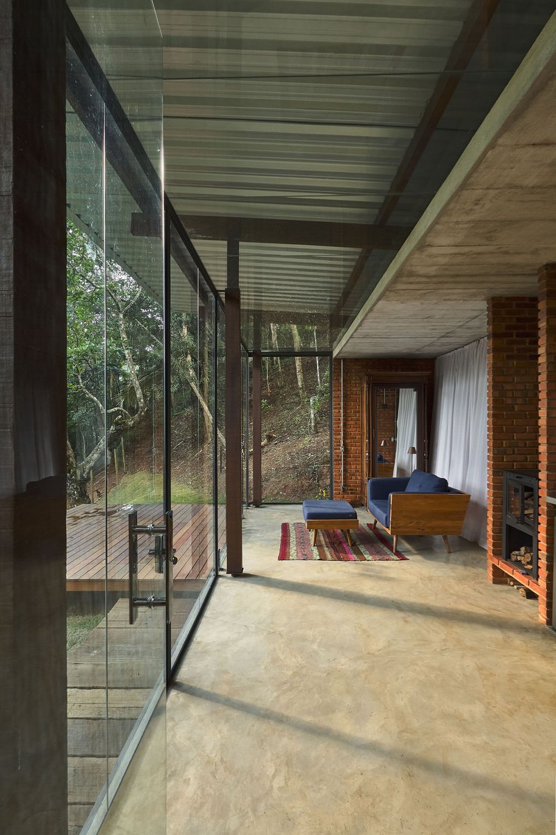 Living space with floor-to-ceiling glass walls revealing timber deck and hillside vegetation under an overcast sky