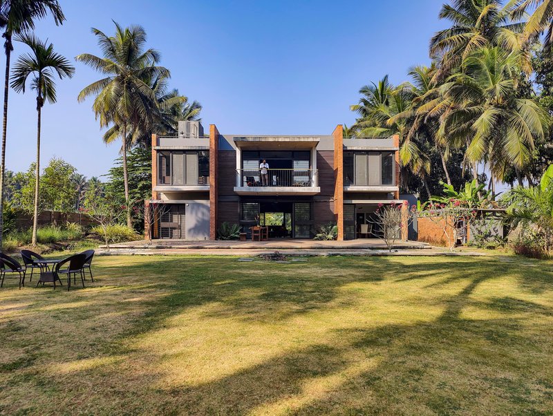 Garden facade with timber and white plaster volumes framed by towering palms under a clear sky