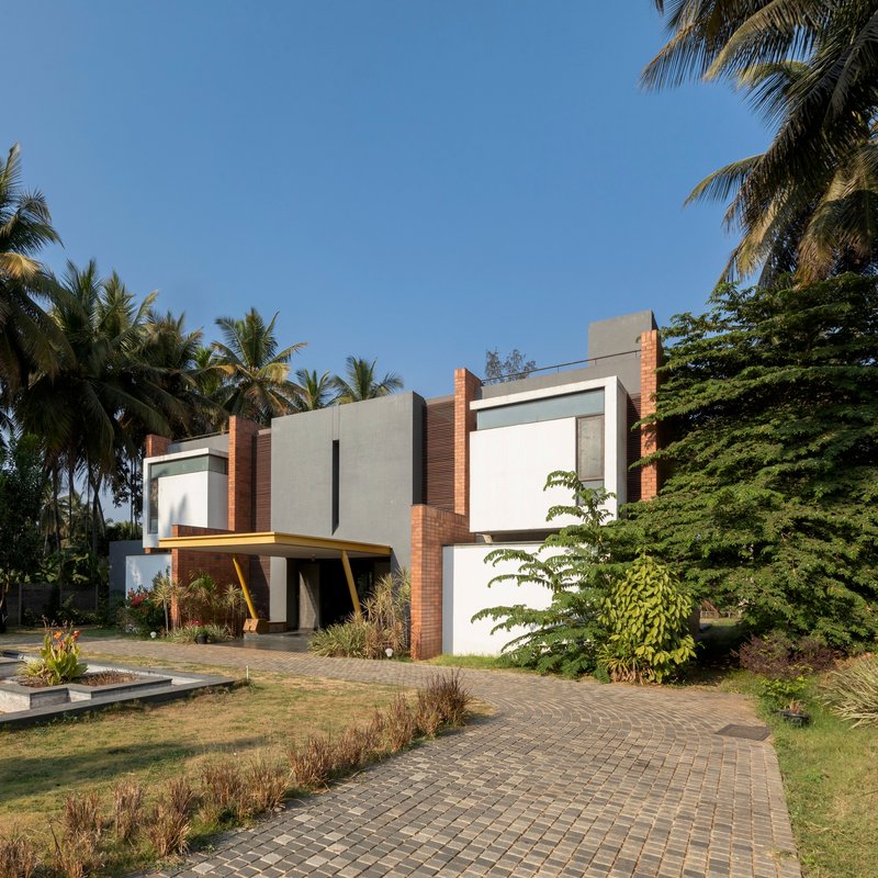 Angled view of the entrance with brick paving and angled yellow canopy amid tropical vegetation