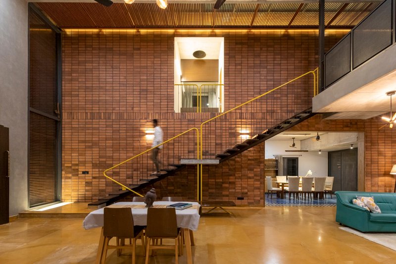 Double-height interior with floating staircase and yellow railing against a patterned brick wall at night