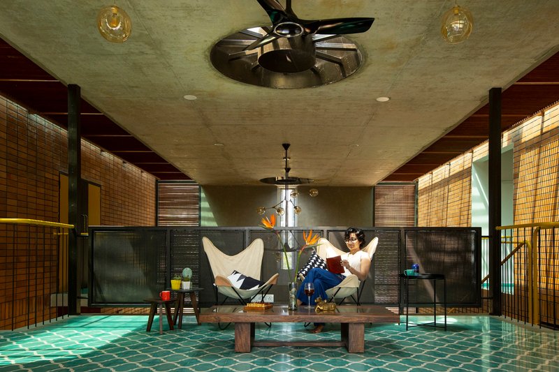 Upper living area with green mosaic floor, slatted timber screens and a seated figure beneath ceiling fans
