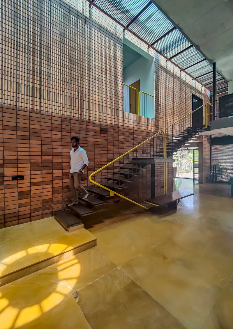 Cantilevered staircase with yellow metal handrail against a terracotta tile wall with a person descending