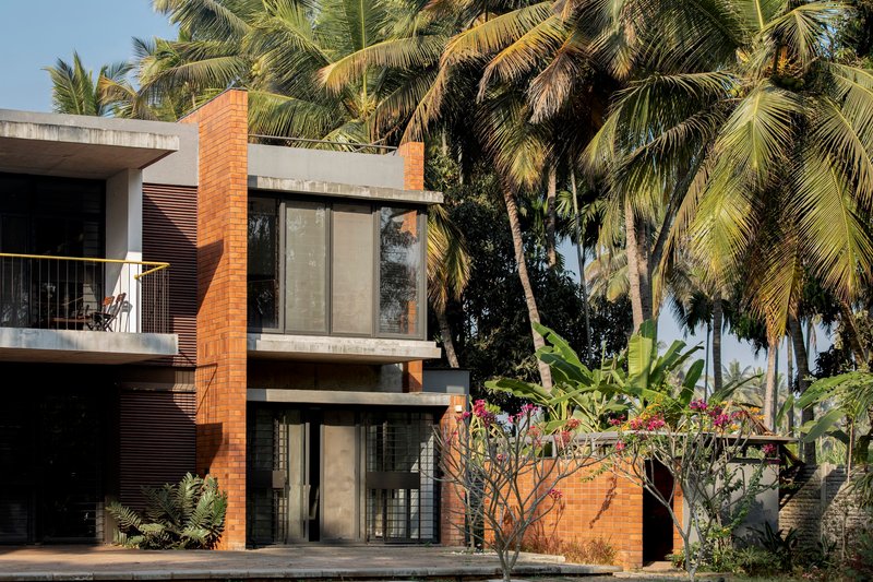 Two-story facade with terracotta brick volumes, concrete slab, and tall glass panels framed by palm trees