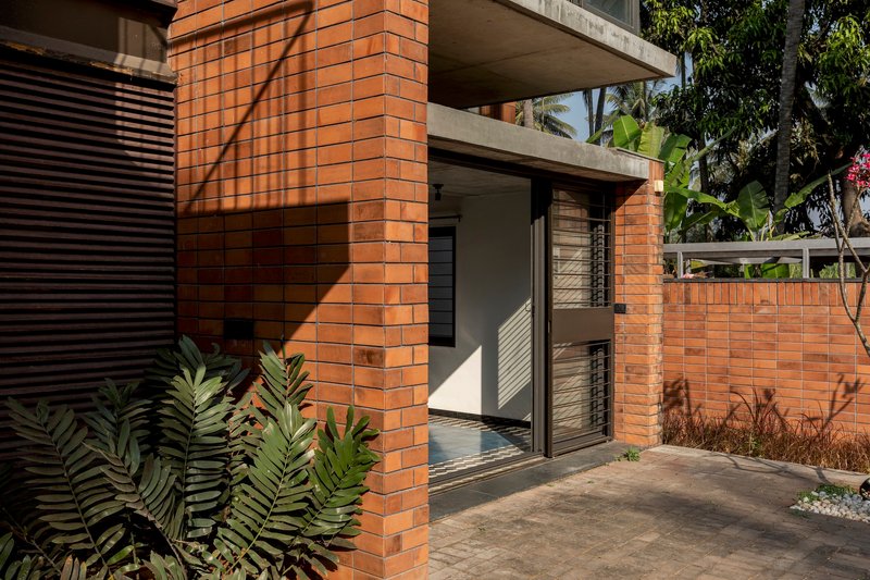 Terracotta brick column and entry threshold with concrete canopy above and morning sunlight on the courtyard
