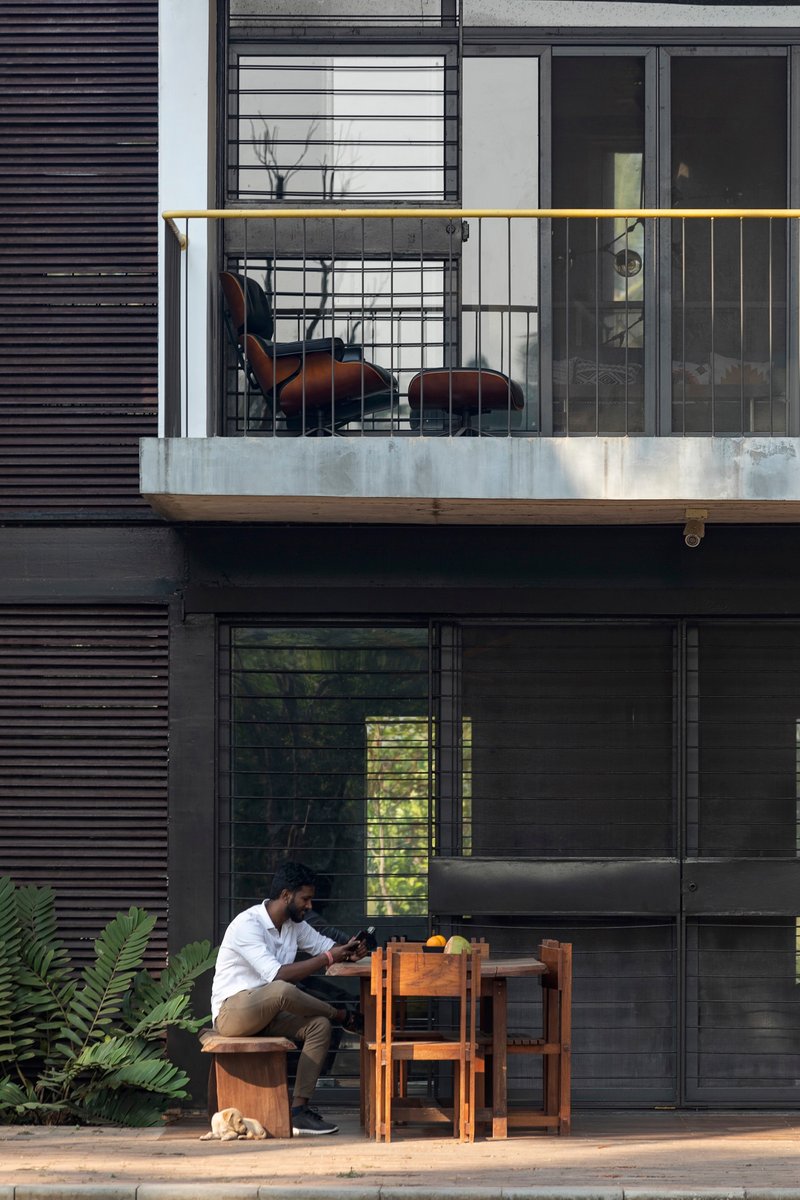 Stacked balconies with horizontal louvers, glass railings, and a resident working at a timber table below