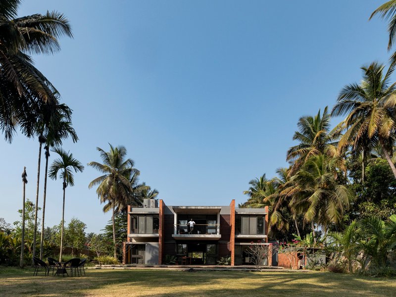 Garden elevation showing the two-story residence with terracotta volumes, glass walls, and palm trees against blue sky