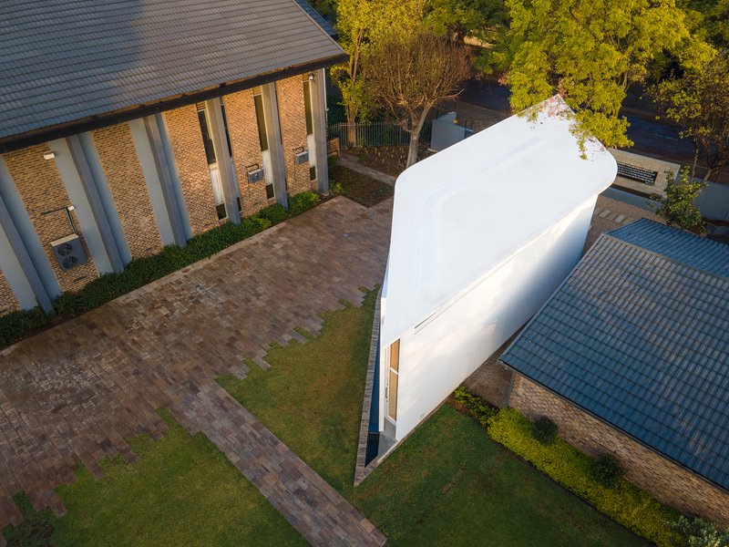 Curved white facade volume standing between brick paver courtyard and neighboring tiled roof buildings at dusk
