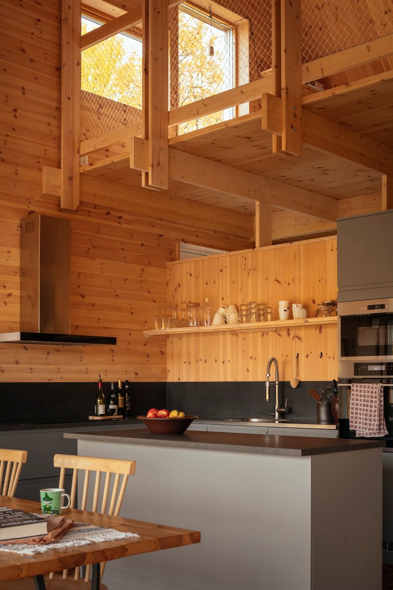 Kitchen island with dark countertop below exposed timber beams and mezzanine level with diamond mesh railing