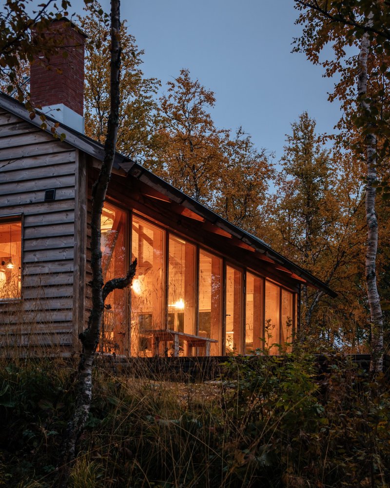 Glazed extension with interior lighting glowing through birch trees at twilight