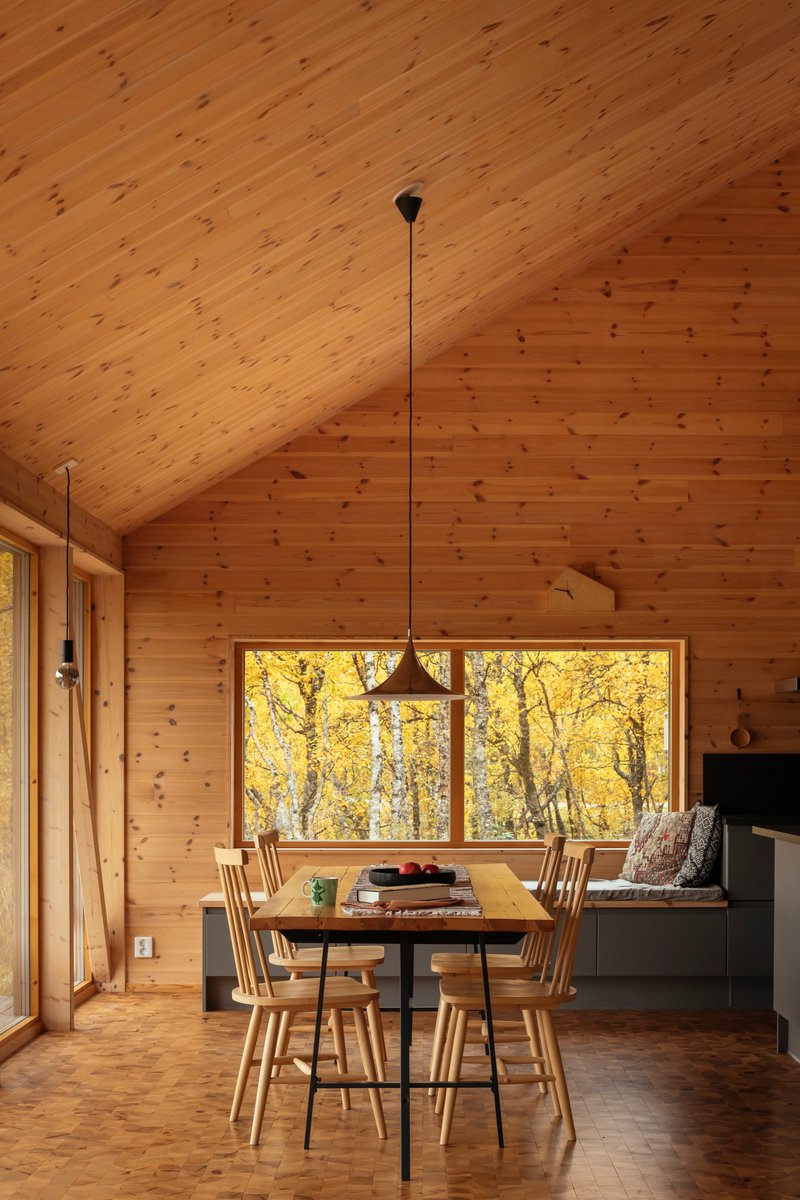 Dining area with wood plank ceiling and horizontal window framing yellow autumn birch trees