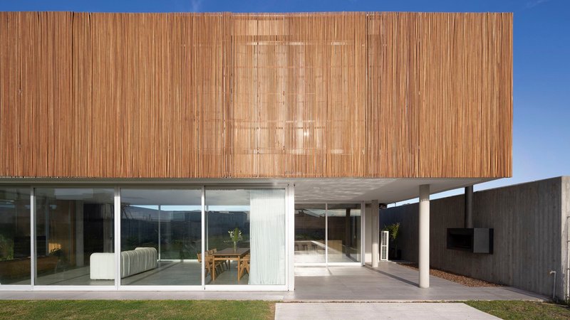 Covered terrace beneath concrete soffit with timber volume above and glass walls opening to interior