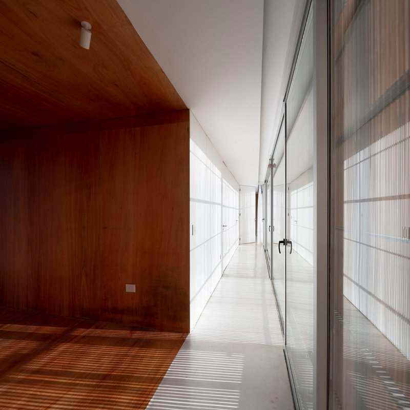 Interior corridor with timber-clad walls and ceiling alongside translucent sliding screens casting linear shadows