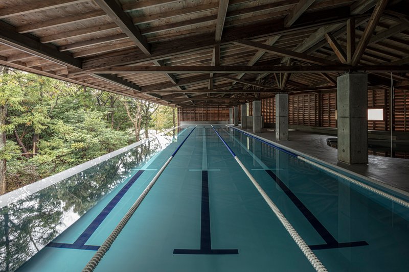 Indoor lap pool with lane markers beneath exposed timber roof trusses and concrete columns