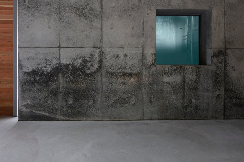 Weathered concrete panel wall with recessed stainless steel window opening and polished grey floor