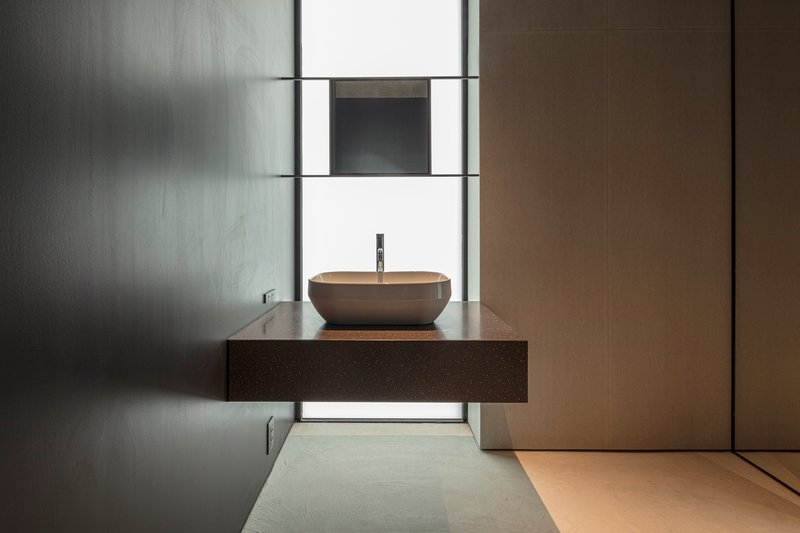 Floating vanity with vessel sink beneath a backlit slot window in polished concrete bathroom