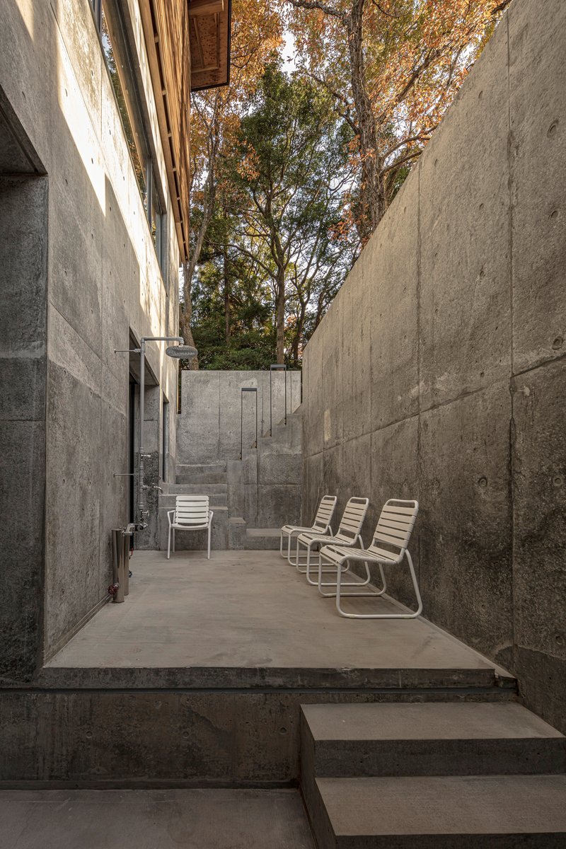 Concrete courtyard with metal lounge chairs flanked by board-formed walls beneath autumn trees