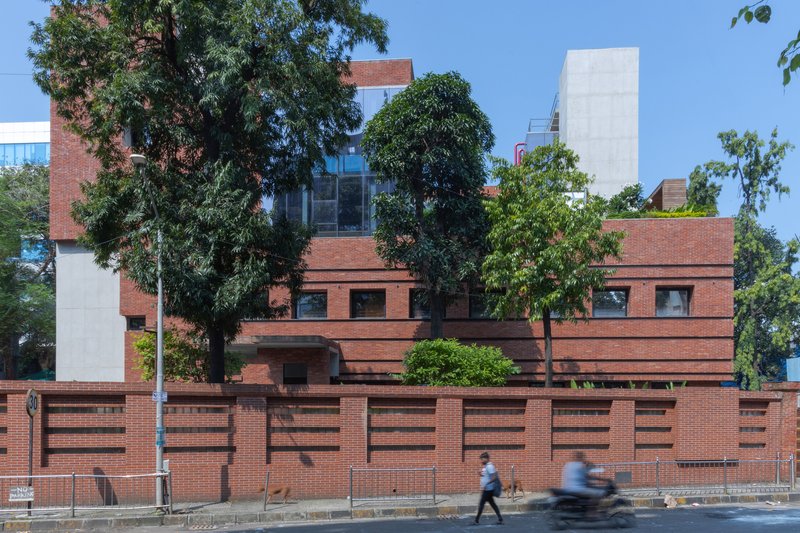 Street view of the layered red brick facade framed by mature trees and pedestrians passing