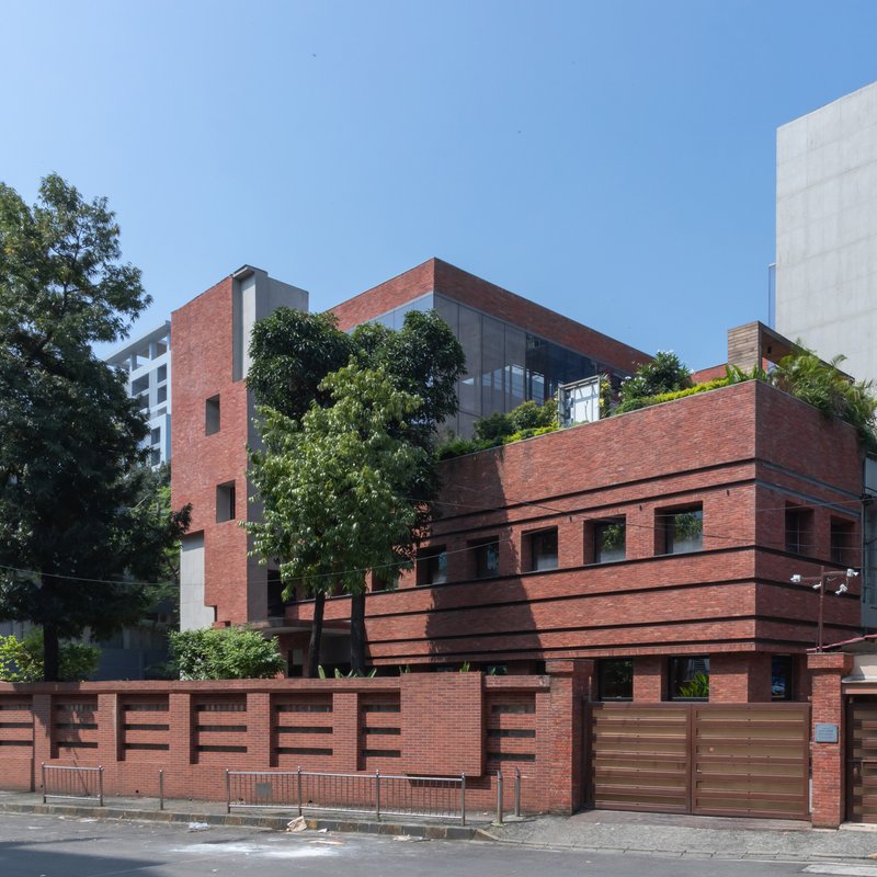 Corner perspective showing the stepped brick volumes with rooftop vegetation and timber gate entry