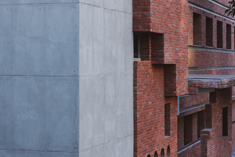 Facade detail showing the junction between smooth concrete panels and textured red brick with recessed openings