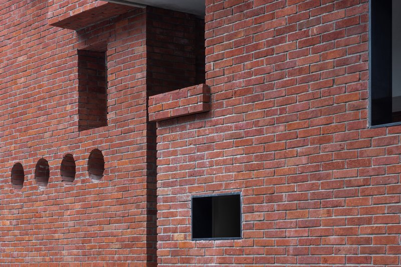 Red brick wall with projecting corbelled elements, recessed niches, and square window openings in afternoon light