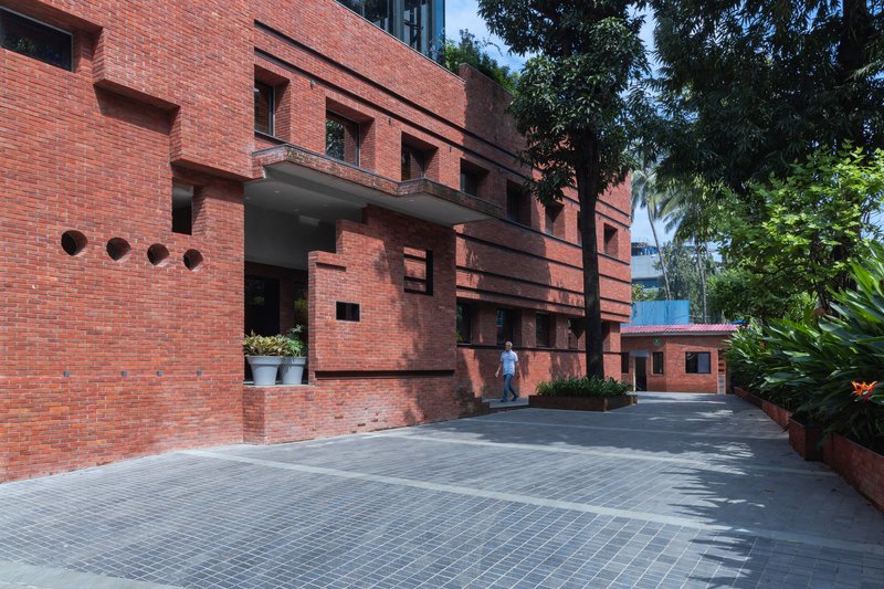 Entry courtyard with red brick facade, covered walkway, and person walking beneath palm trees