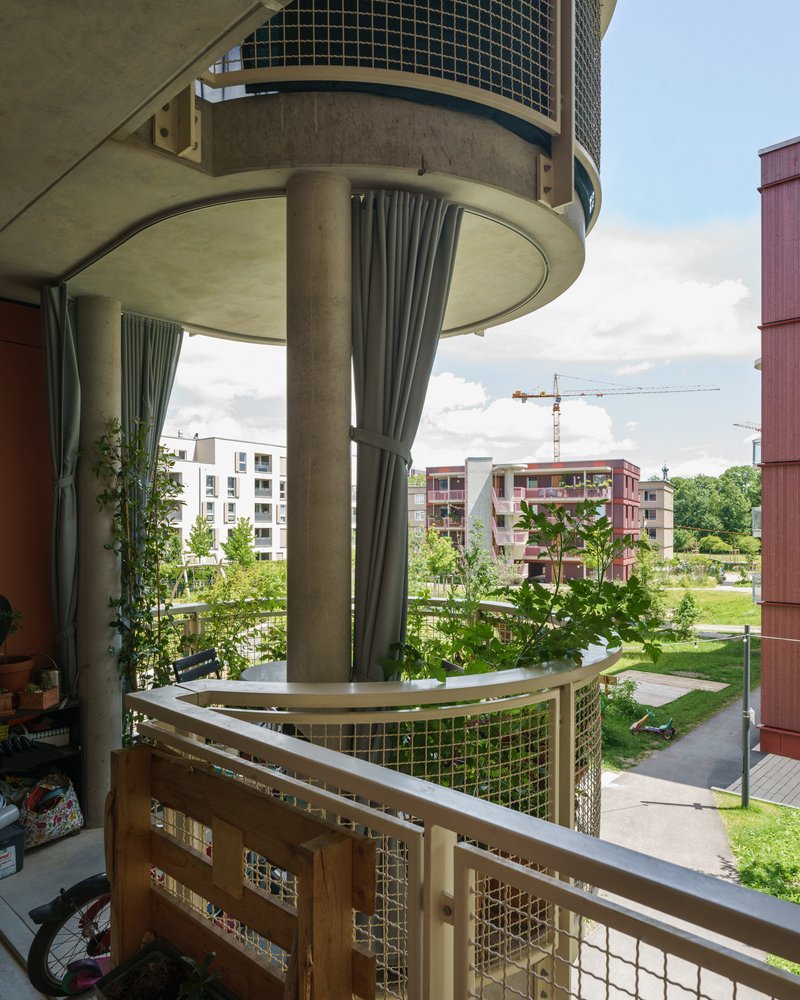 Circular balcony with mesh railing and concrete column supporting the cantilevered slab above overlooking landscaped grounds