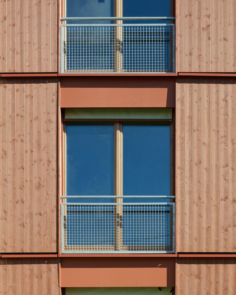 Facade detail showing stacked balconies with mesh railings framed by vertical timber cladding