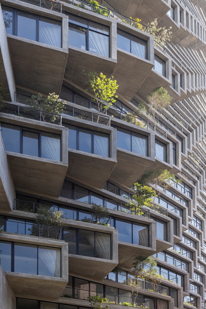 Stacked concrete balconies with planted trees and floor-to-ceiling glazing in bright daylight