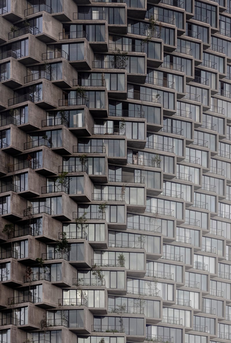 Repetitive concrete balcony grid with recessed glass panels and scattered vegetation