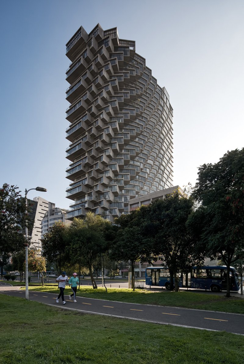 View of the spiraling tower from the park pathway with pedestrians and surrounding trees at dusk