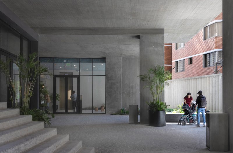 Covered entry courtyard with board-formed concrete ceiling and family with stroller walking past potted palms