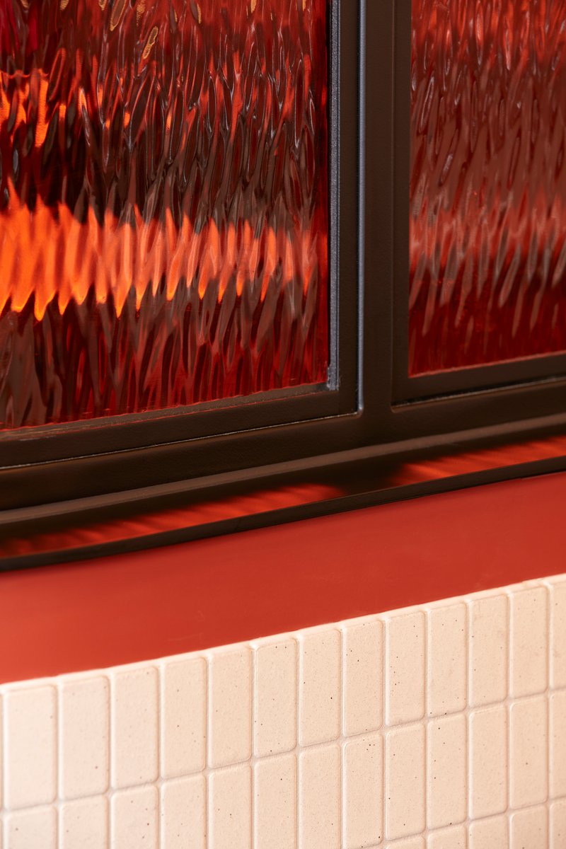 Textured glass window above white tile wainscoting with red wall and sill in warm interior light
