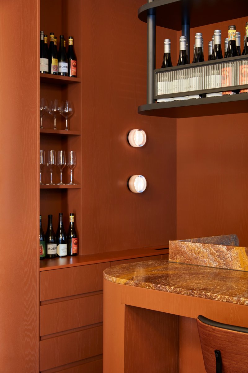 Bar area with timber shelving and suspended bottle rack above terrazzo-topped counter under wall sconces