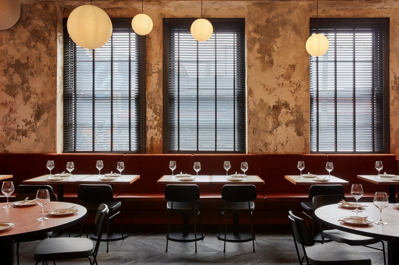 Banquette seating along windows with venetian blinds and sphere pendants above set tables